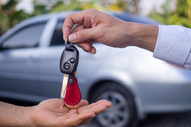 De verkoper stuurt de autosleutels naar de hand van een vrouwelijke klant. Na ondertekening van het contract tussen aankoop - verkoop succesvol