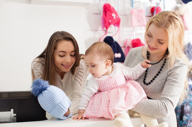 De verkoper toont een winterblauwe meisjesmuts met pompon om aankopen te selecteren