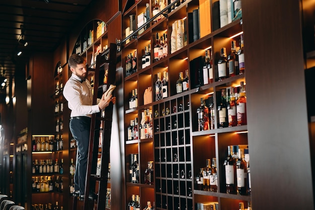 De verkoper van alcoholische dranken sorteert flessen die op de ladder staan.