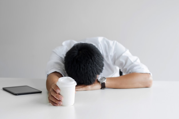 De vermoeide bedrijfsmens neemt een dutje met koffie op het werk