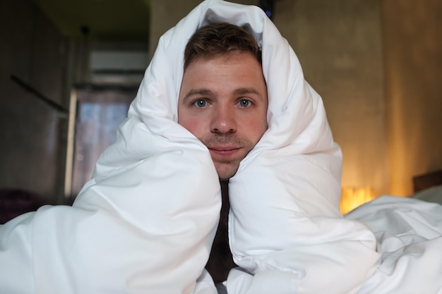 Foto de vermoeide blanke man lag op het bed en kijkt met mooie ogen vooruit