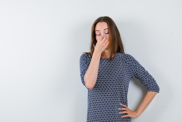 De vermoeide vrouw denkt door haar neus met hand op witte achtergrond te houden