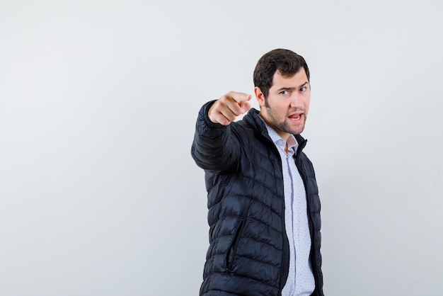 De verraste jonge man wijst naar de camera met wijsvinger op witte achtergrond