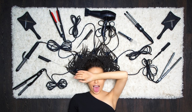 De verrukkelijke meisjeskapper bedekte haar gezicht met haar hand en stak haar tong uit. op de achtergrond zijn er accessoires voor kapsels en kappers