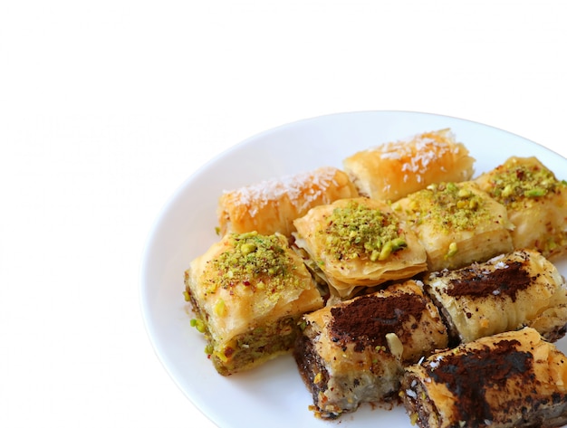 De verscheidenheid van mouthwatering Baklava-gebakjes diende op witte die plaat op witte achtergrond wordt geïsoleerd