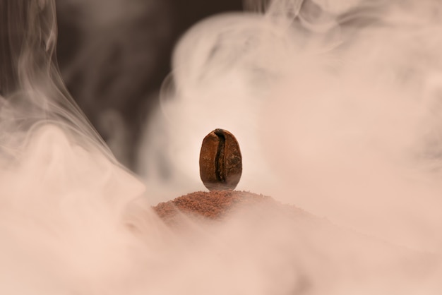 De verse geroosterde koffieboon bevindt zich op een verstrooiing van grondkoffie in de rook