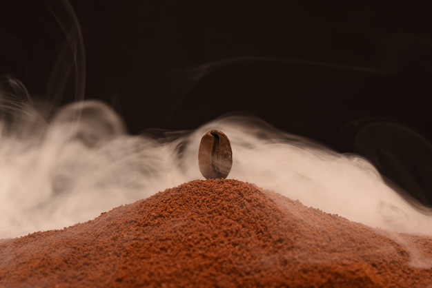 De verse geroosterde koffieboon bevindt zich op een verstrooiing van grondkoffie in de rook