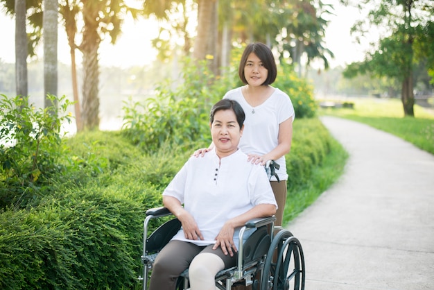 De verzorger behandelt bejaarde Aziatische vrouwenzitting op rolstoel bij openbaar park, het Hogere concept van de zorgverzekering