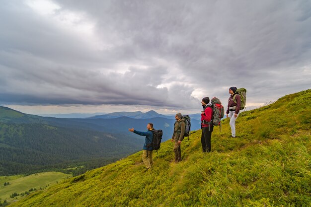 De vier actieve mensen met rugzakken die op de groene berg staan