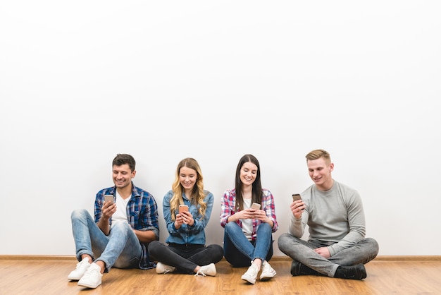 De vier gelukkige mensen zitten op de grond en bellen op de witte achtergrond