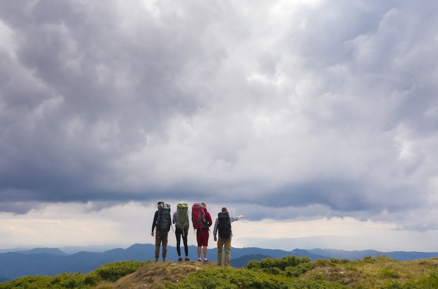 De vier mensen met rugzakken staan op een berg tegen prachtige wolken