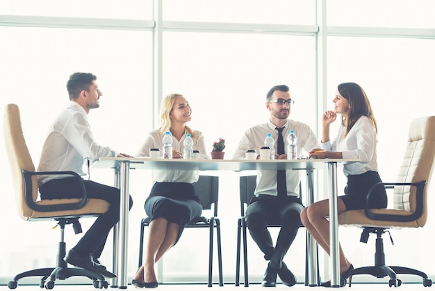 De vier zakenmensen zitten aan de kantoortafel bij het panoramische raam