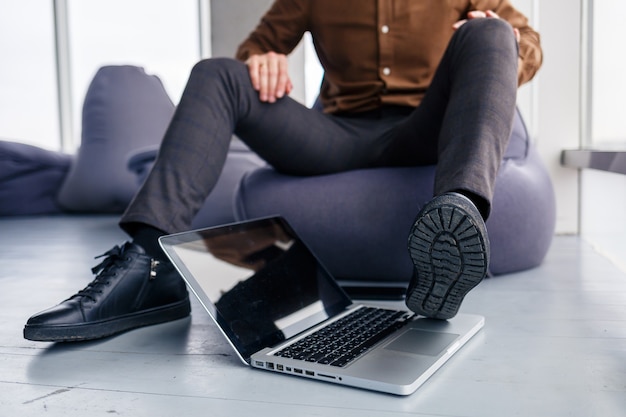 De voet van een man in schoenen is in de buurt van de laptop