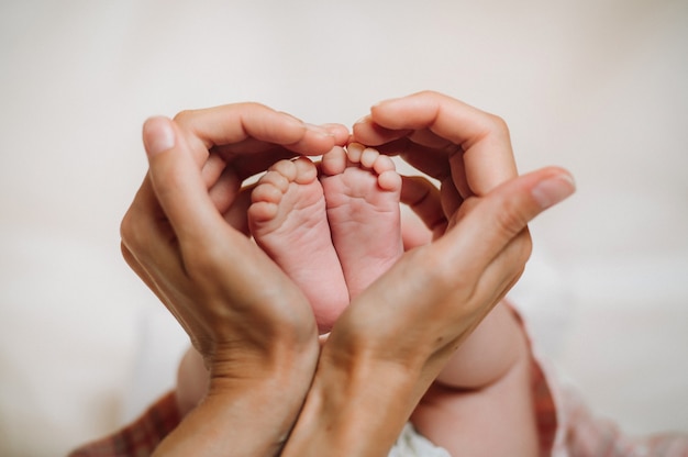 De voeten van de pasgeborene in de handen van de moeder houden de vorm van een hart vast. kindervoeten in de handen van de moeder.