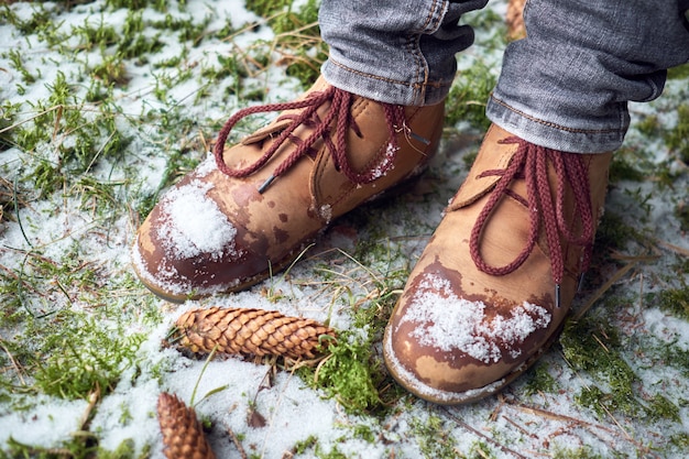 De voeten van de vrouw in reislaarzen op een bemoste sneeuwgrond in de winterbos. Reizen concept.