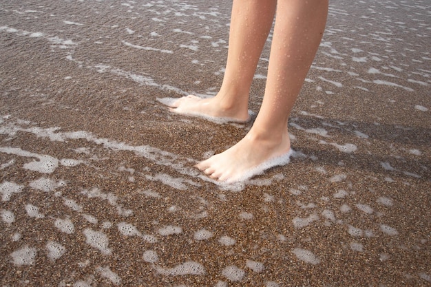 De voeten van een jongen op het zand op het strand gewassen door de zee