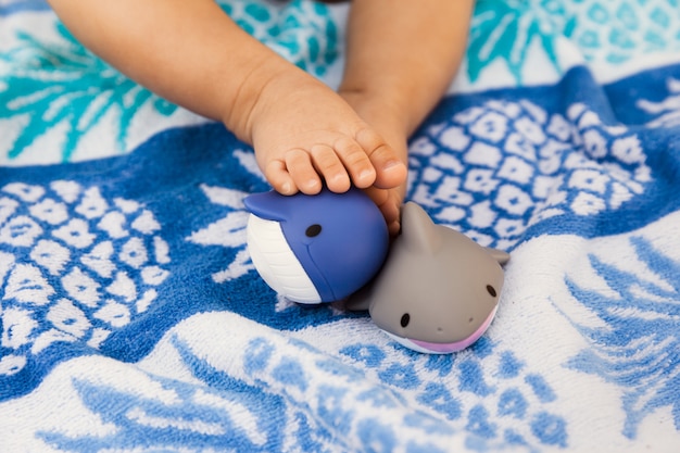 Foto de voeten van het babymeisje met rubberspeelgoed op de zomerhanddoek