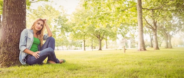 Foto de volledige lengte van glimlachende vrouw met dient haar in terwijl het zitten onder boom