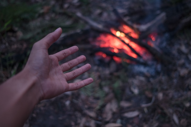 De volwassen man verwarmt handen rond het kampvuur in het bos.