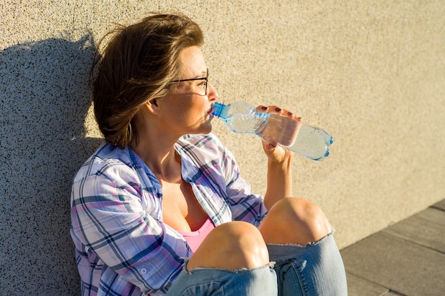 De volwassen vrouw met glazen is drinkwater van fles