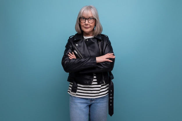 De volwassen vrouw van middelbare leeftijd met grijs haar in een stijlvolle jeugdlook ziet er cool uit op een blauw