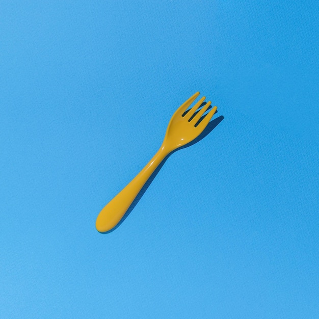 De vork is gemaakt van geel plastic in een felle kleur op een blauwe achtergrond Plat gelegd