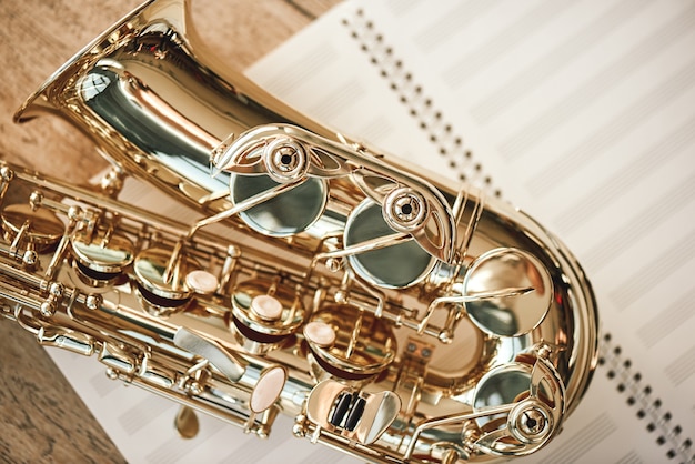 De vreugde van sax. Bovenaanzicht van mooie glanzende saxofoon liggend op bladen voor muzieknoten over houten vloer. Muziekinstrumenten. Muziek apparatuur.