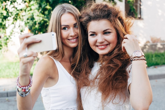 Foto de vrij jonge meisjes die selfie openlucht op de straat in de zomermeisjes doen hebben pret met smartphone die selfie doen