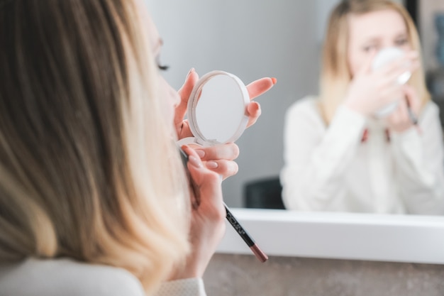 De vrij jonge vrouw schildert lippen kijkend in compacte spiegel