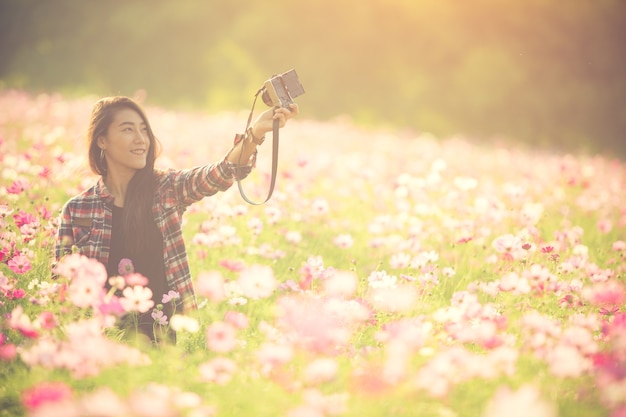 De vrij jonge vrouwelijke toerist neemt reis selfie bij het gebied van de kosmosbloem.