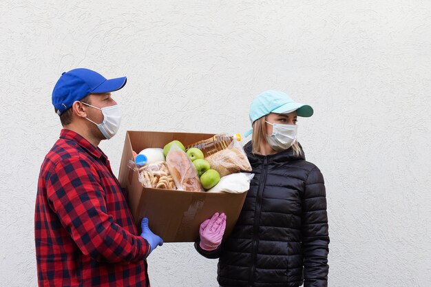 De vrijwilligers in beschermende maskers met een doos met eten