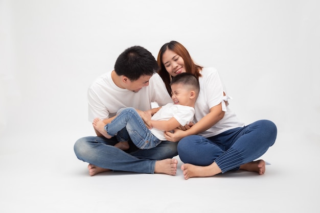 De vrolijke Aziatische familiezitting over witte muur heeft pretvader die weinig zoon kietelt. Jong koppel met kinderen dragen witte top en spijkerbroek. Ouders genieten van het concept van vrije tijd spelen