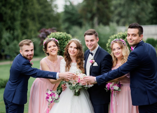 De vrolijke bruid en de bruidegom en hun vrienden drinken champagne in het park