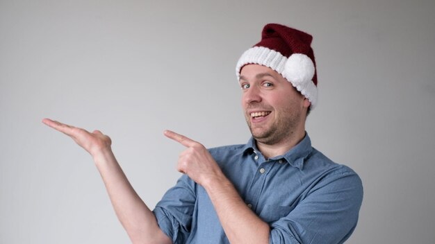 De vrolijke europese jongeman met een nieuwjaarshoed wijst naar een lege ruimte waar een product wordt gepresenteerd
