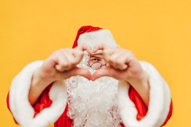 De vrolijke kerstman die een mooie bril draagt, toont een liefdesgebaar