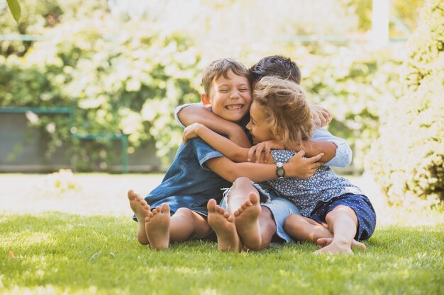 De vrolijke kleine kinderen zitten op een groen grasveld en knuffelen samen