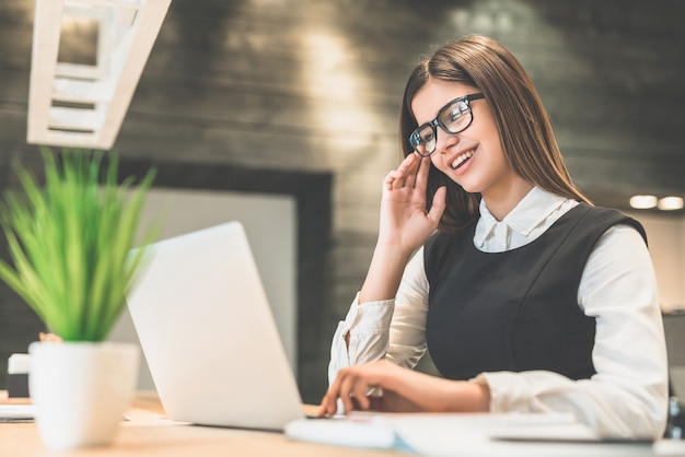 De vrolijke vrouw met een moderne laptop aan de desktop