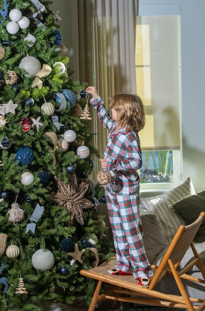 De vrolijke zoon van het Kerstmiskind die huis voor de Kerstmiskerstboom van de Kerstmisviering in de achtergrondkerstmis voorbereiden
