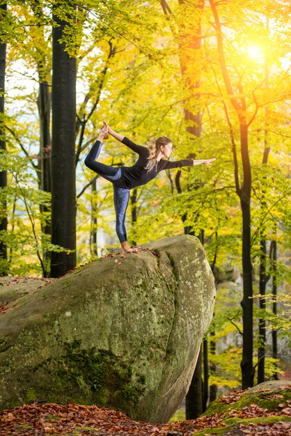 De vrouw beoefent yoga in de herfstbos op de grote steen