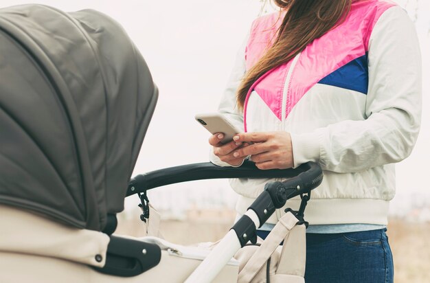 De vrouw checkt sociale netwerken in haar telefoon terwijl ze met de kinderwagen loopt