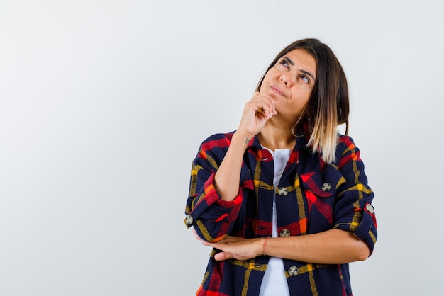 De vrouw denkt door haar hand op de kin op een witte achtergrond te leggen