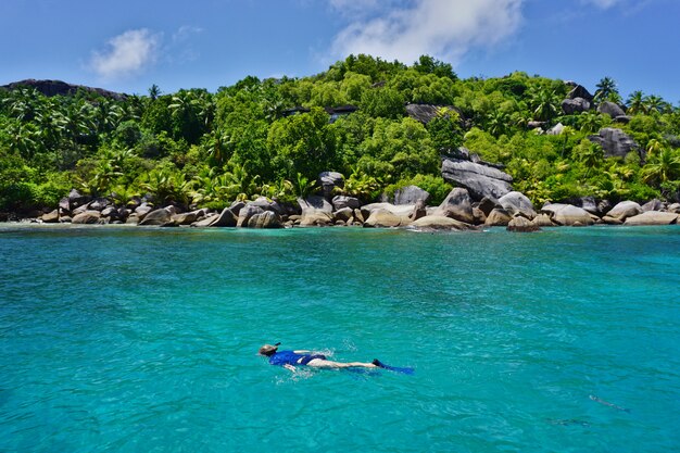 De vrouw die blauw materiaal draagt snorkelt in de turkooise blauwe wateren van een paradijseiland.