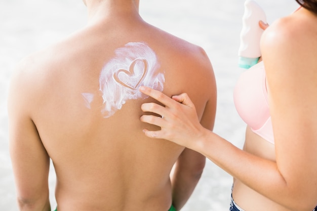 De vrouw die een hartsymbool maken bemant terug terwijl het toepassen van een zonneschermlotion