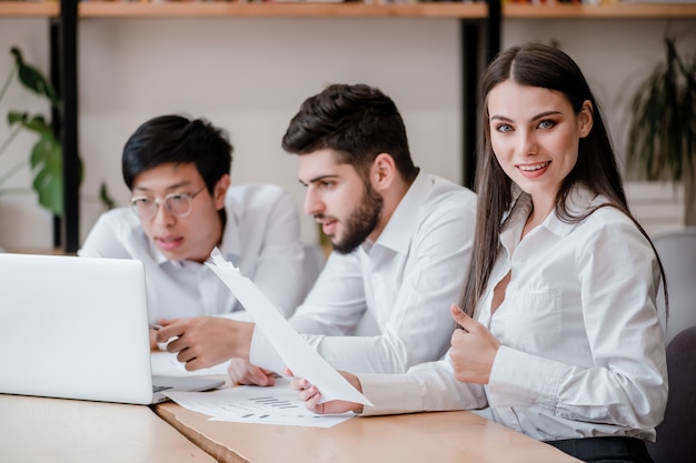 De vrouw die in het bureau werkt toont duimen met diverse mannelijke medewerkers