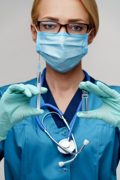 De vrouw die van de medische artsenverpleegster beschermend masker dragen en handschoenen die spuit houden