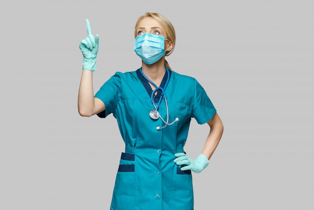 De vrouw die van de medische artsenverpleegster beschermend masker en latexhandschoenen dragen - benadruk een vinger op lege copyspace