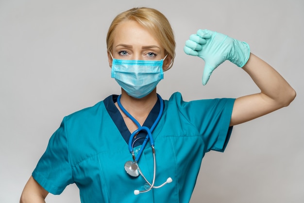 De vrouw die van de medische artsenverpleegster beschermend masker en latexhandschoenen dragen - die grote duim neer tonen