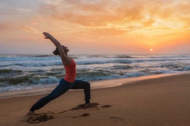 De vrouw die yogaasana Virabhadrasana 1 doen Strijder stelt op strand