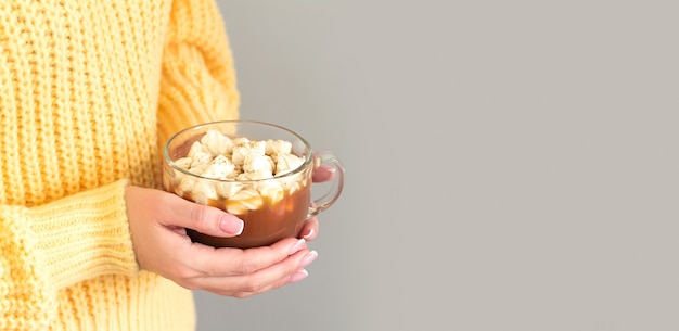 De vrouw draagt een gele trui en houdt een grote mok warme chocolademelk of chocolade met marshmallow vast