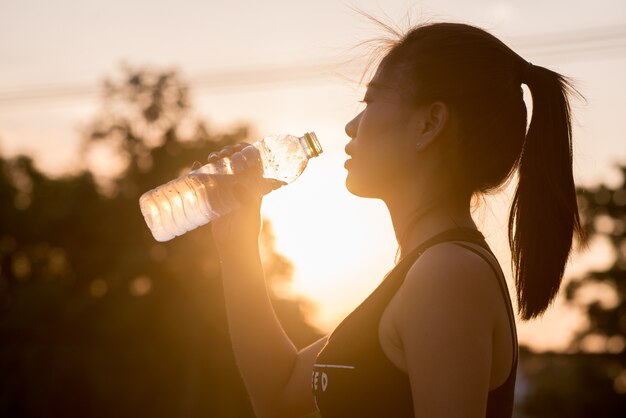 De vrouw drinkt water op zonsondergangachtergrond